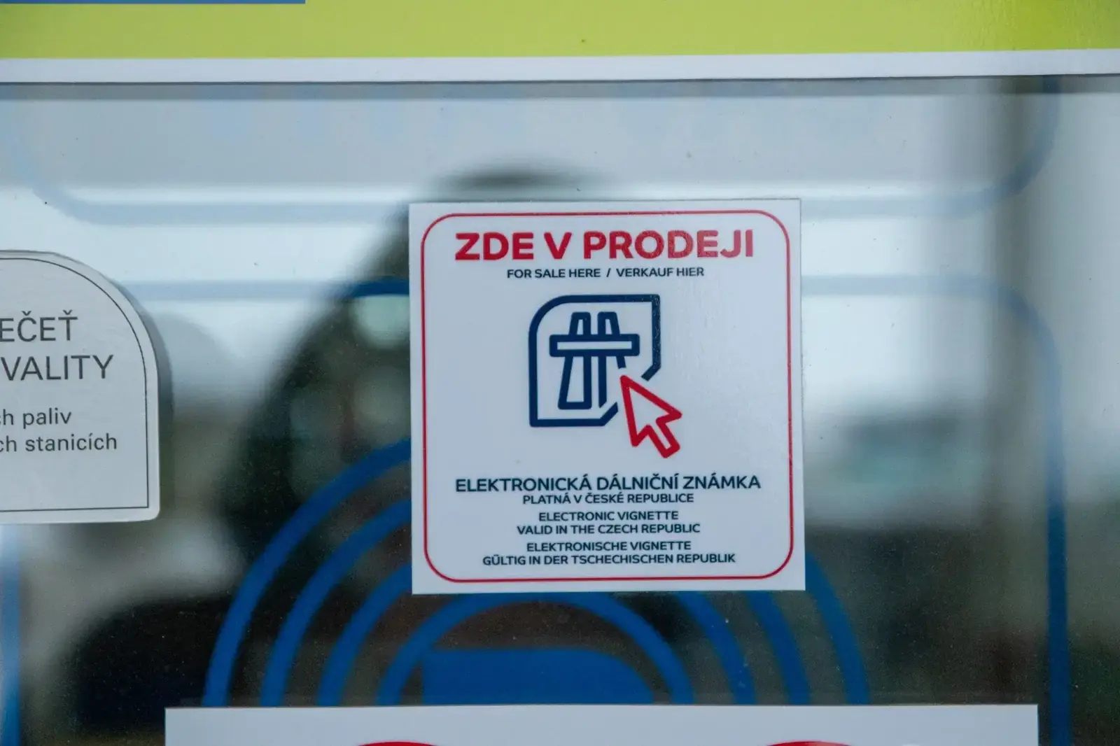 Point-of-sale sticker showing where to buy a Czech electronic highway vignette (e-známka) at a petrol station, with text in Czech, English and German