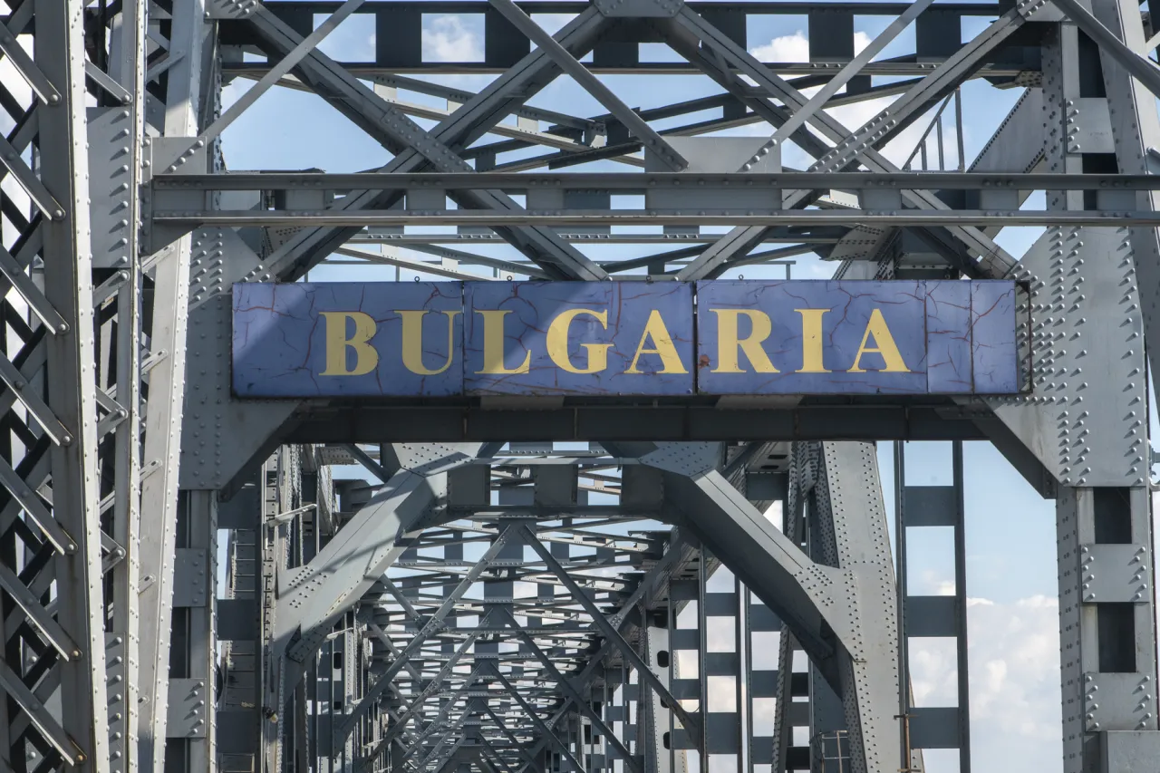 Close-up of weathered gold Bulgaria entry sign mounted on historic steel truss Danube Bridge structure against blue sky