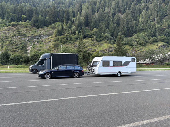 Car towing a caravan with bicycles on the Brenner Autobahn in Austria, with truck and forested Alpine mountains in the background