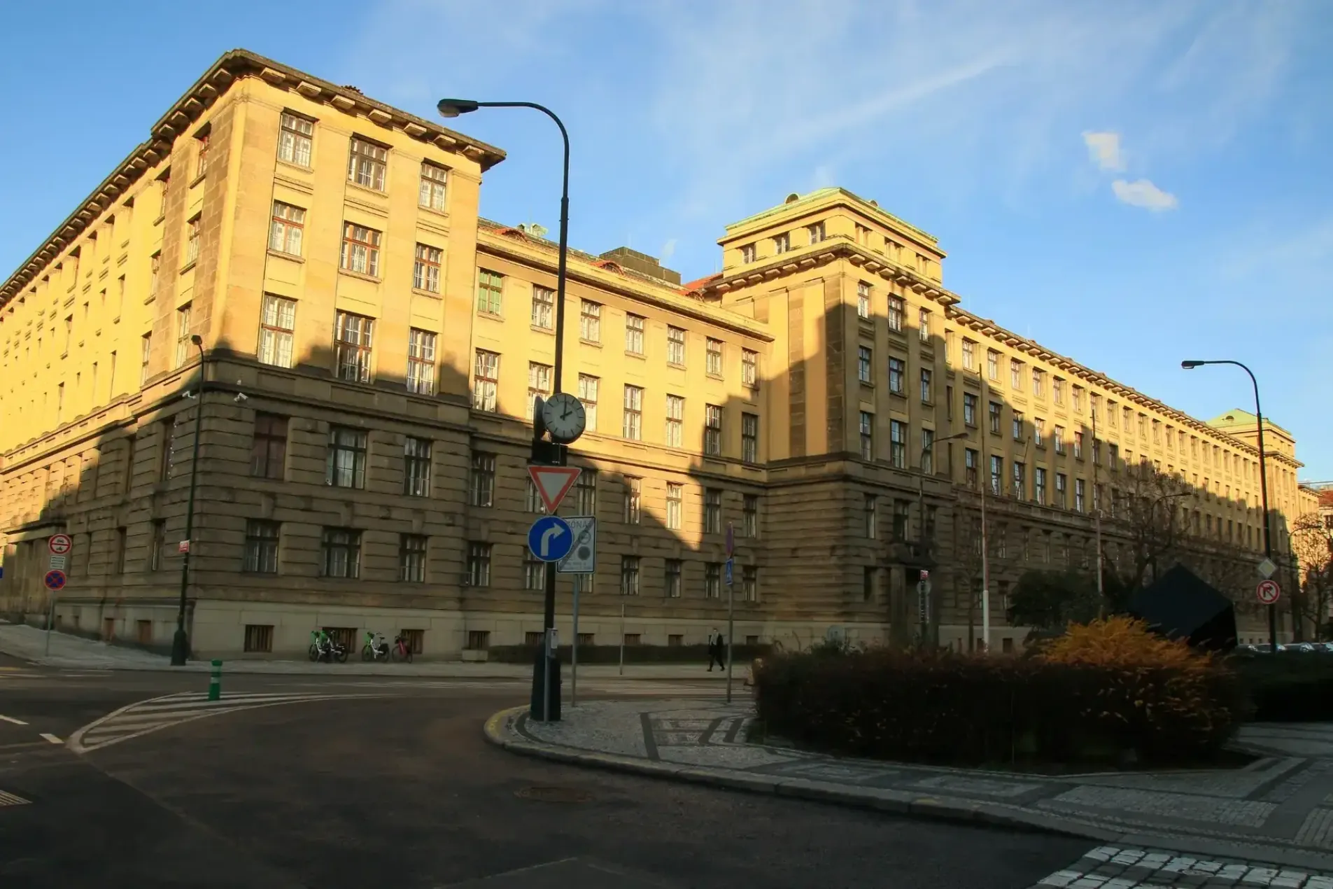 Ministry of Transport building in Prague, Czech Republic, illuminated by golden winter sunlight with a street clock and road signs at a city intersection – December 2025